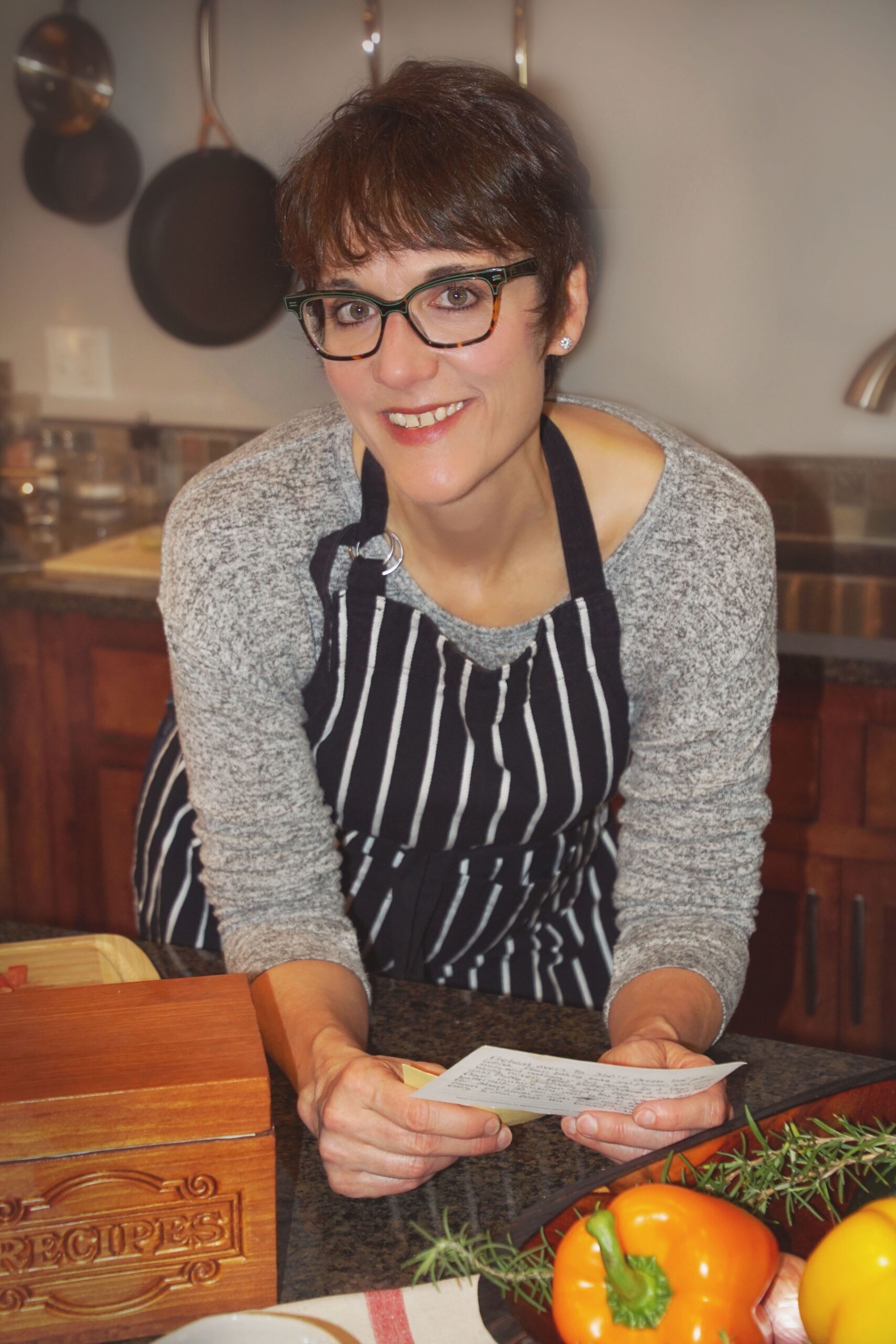 Cheryl Englebretson smiles at the camera wearing a chef's apron and a recipe card.