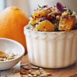 Quinoa Orange Fennel Beet in white bowl with orange and sunflower seeds on wood cutting board