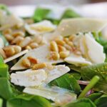 Shaved parmesan and pine nuts on top of baby arugula greens.