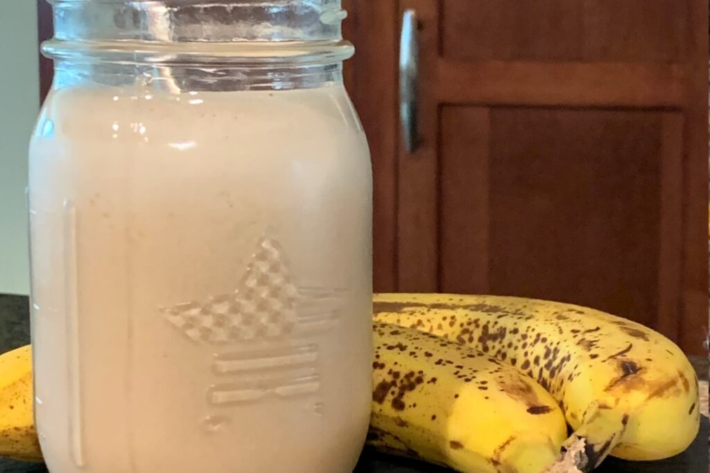 banana nut or seed butter smoothie in mason jar with stainless straw on slate with bananas.