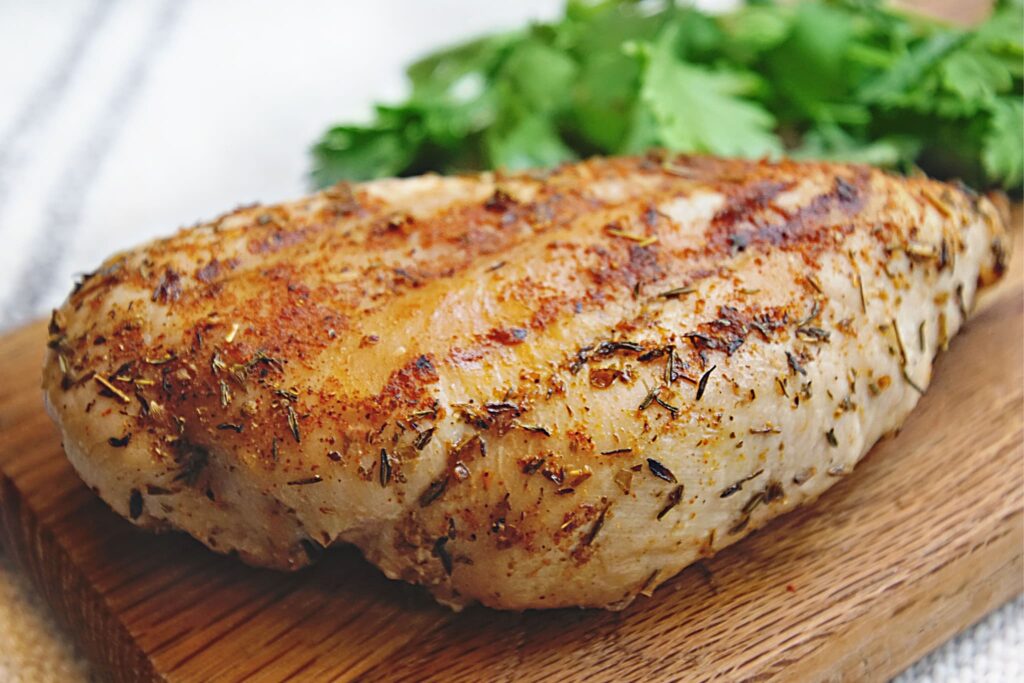 seasoned grilled chicken on wood board with herbs.
