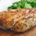 seasoned grilled chicken on wood board with herbs.