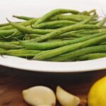 roasted haricots verts on white plate and wood table with garlic cloves and lemon.