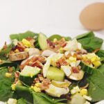 spinach salad with bacon, egg, cucumber and mushroom on white background.