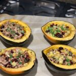 Acorn squash stuffed with meat vegetables and cranberries on parchment lined baking sheet.