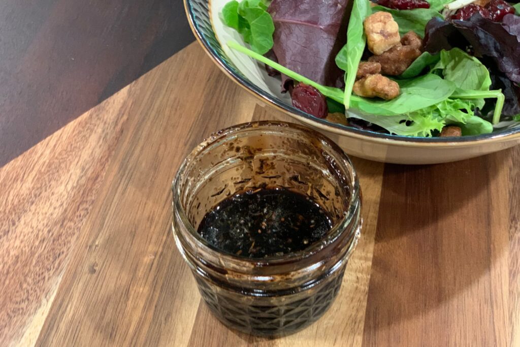 balsamic and herb vinaigrette in small mason jar on wood board with mixed green salad.