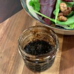 balsamic and herb vinaigrette in small mason jar on wood board with mixed green salad.