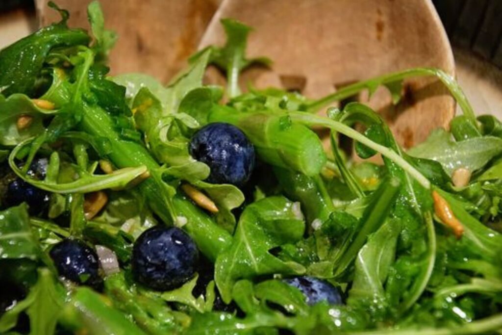 arugula, asparagus, blueberry salad with wooden salad spoons.