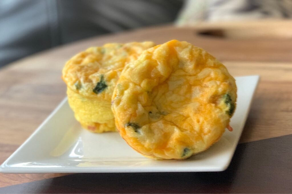 Spinach and cheese egg bake muffins sit on a white square plate on a wooden cutting board.