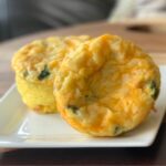 Spinach and cheese egg bake muffins sit on a white square plate on a wooden cutting board.