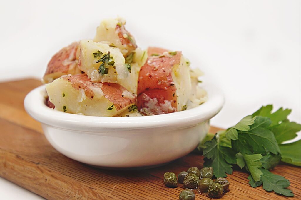 herbed potato salad with capers on cutting board with white background.
