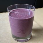 peach and blueberry smoothie in glass on light yellow cloth.