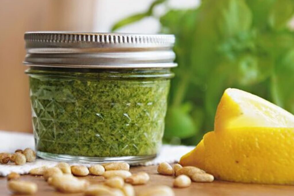 pesto in glass jar with lid lemon slices and pine nuts.