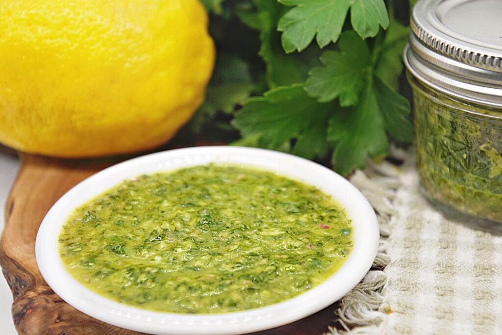 chimichurri sauce in white bowl with parsley and lemon.