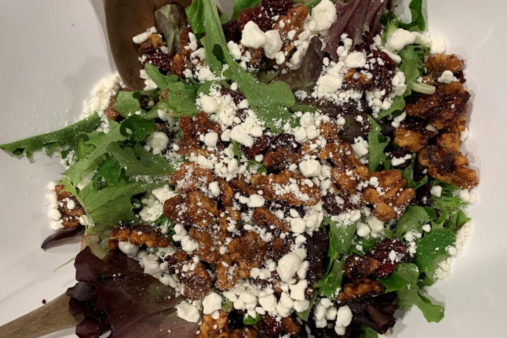 Mixed greens glazed nut, dried cherries goat cheese in white bowl.
