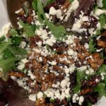 Mixed greens glazed nut, dried cherries goat cheese in white bowl.