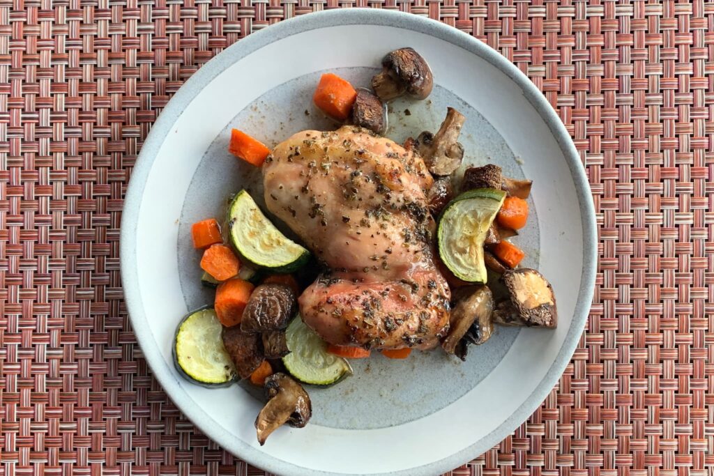 Chicken Thighs with baked vegetables on grey plate and weaved place mat.