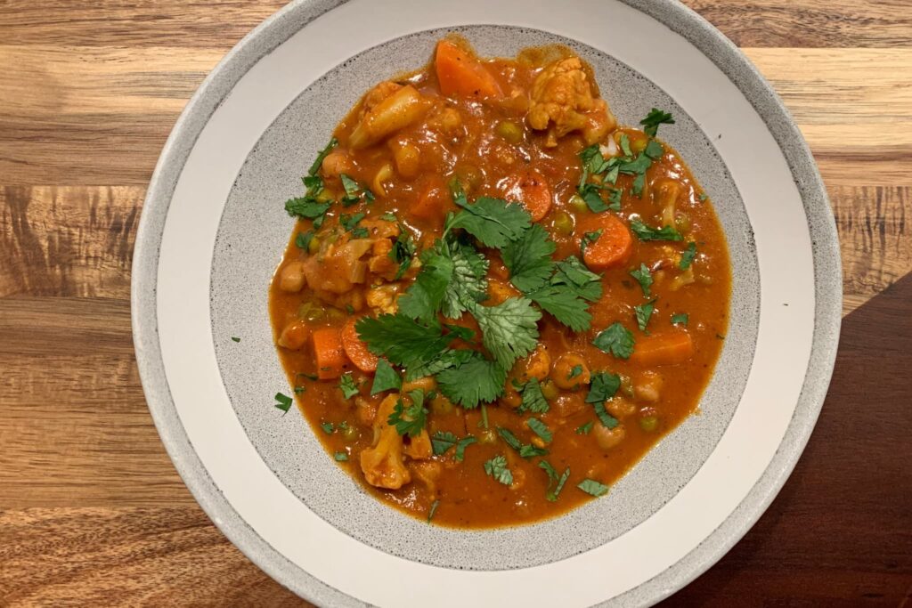 Vegetable Tikka Masala with cilantro in a gray and white bowl on wood board.