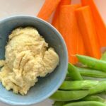 Artichoke dip in blue bowl with carrots and snap peas.