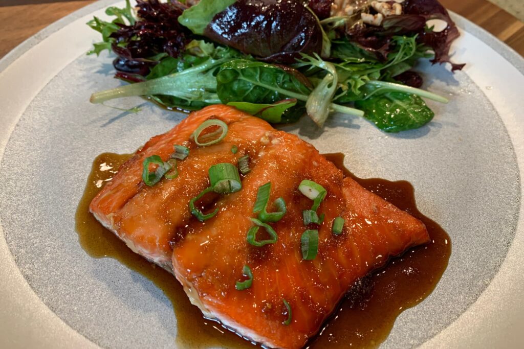 Maple marinated Salmon with Green Onion and salad on gray plate.