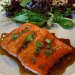 Maple marinated Salmon with Green Onion and salad on gray plate.