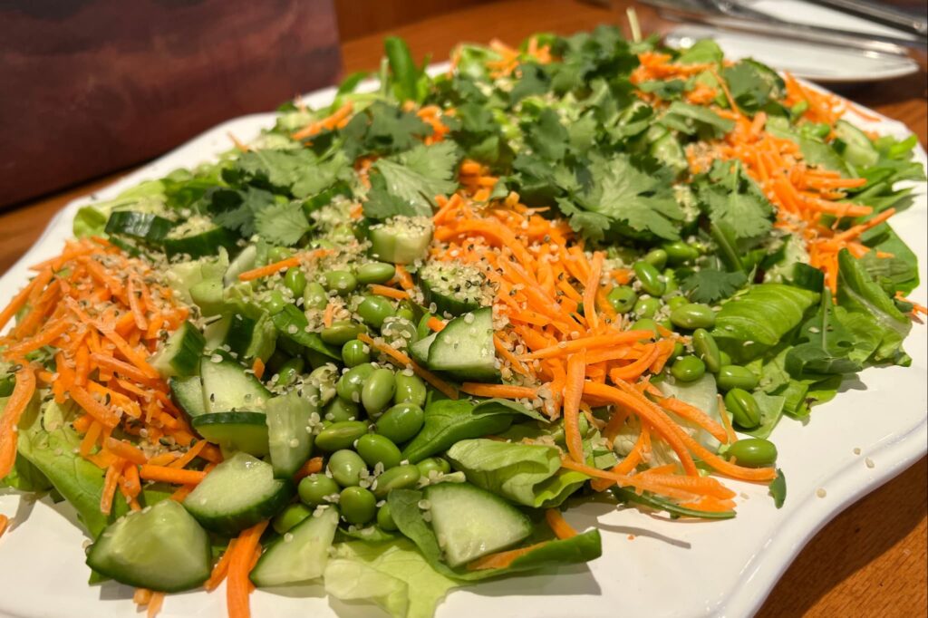 Greens salad with carrots edamame and cucumber on white serving platter.