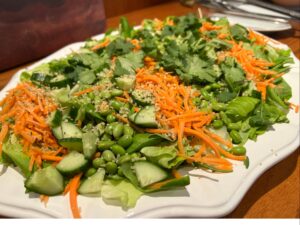 Greens salad with shredded carrots, cucumbers and edamame on white platter.