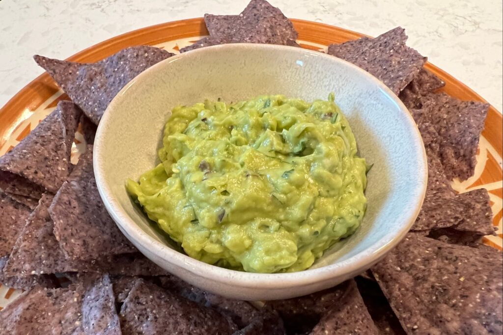 guacamole in white bowl with blue corn tortilla chips.