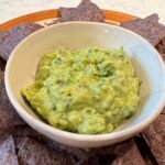 guacamole in white bowl with blue corn tortilla chips.