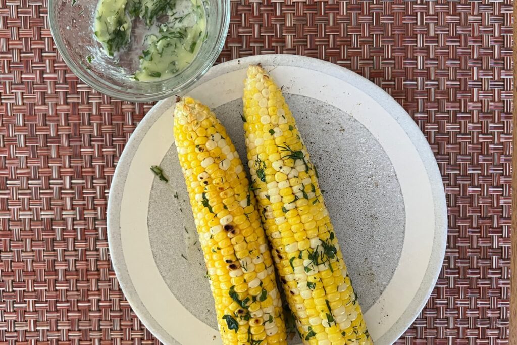 grilled corn on the cob on plate with herb butter.
