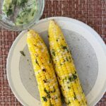 grilled corn on the cob on plate with herb butter.