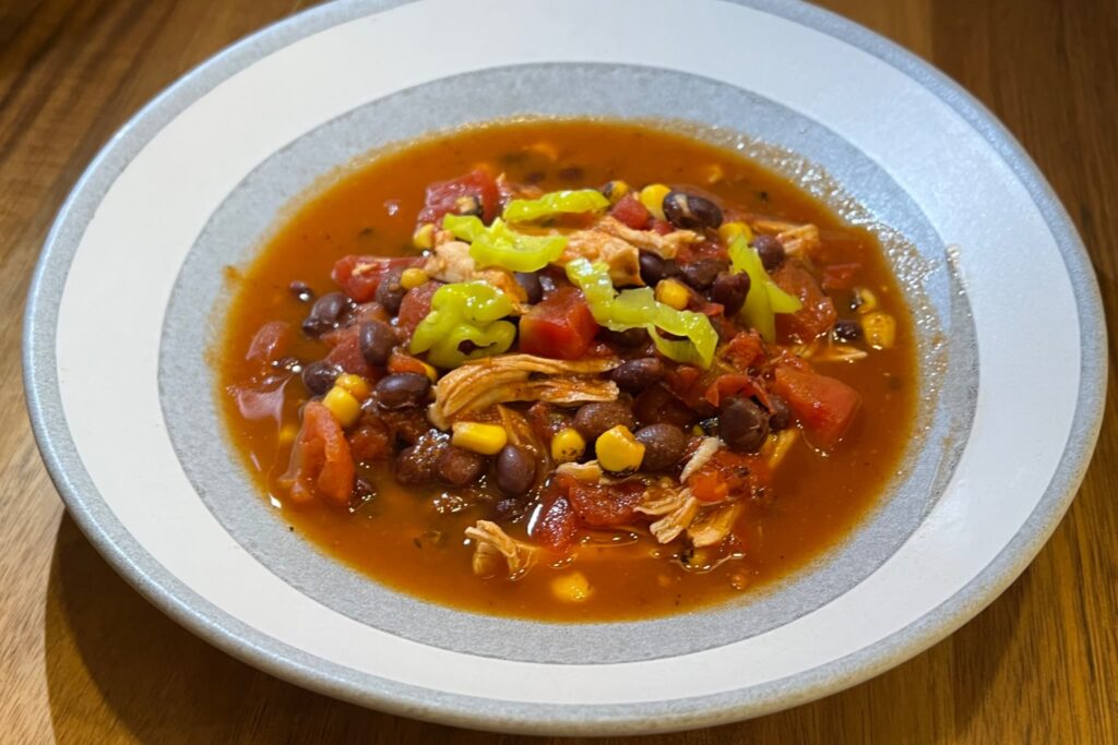Chicken taco soup with toppings in gray bowl on wood table.