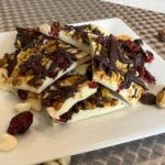 white chocolate bark with fruit and nuts on white plate.