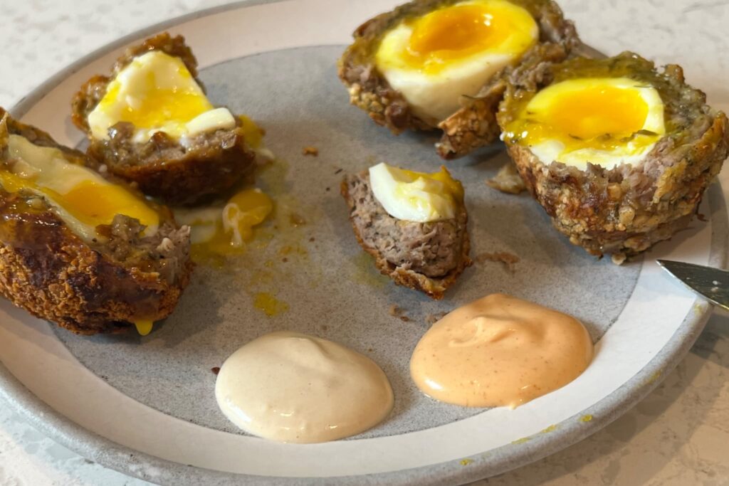 Scotch eggs on gray plate with dipping sauces.