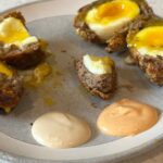 Scotch eggs on gray plate with dipping sauces.