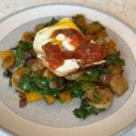 Breakfast skillet dish full of veggies and topped with an egg.