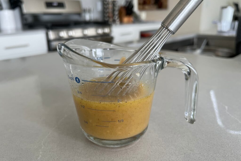 Vinaigrette in glass measuring cup with whisk.