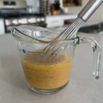Vinaigrette in glass measuring cup with whisk.