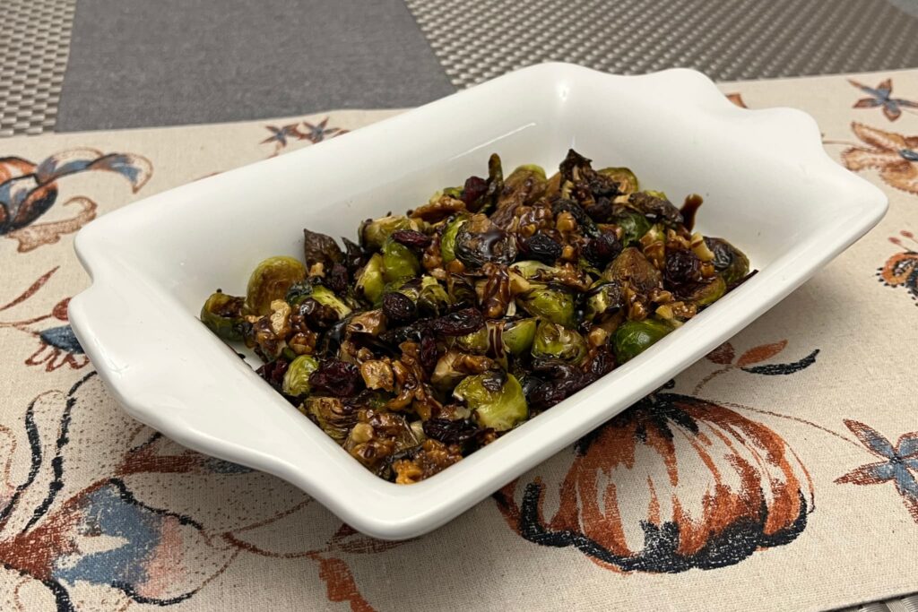 Brussel Sprouts with dried cherries and walnuts in white serving dish.